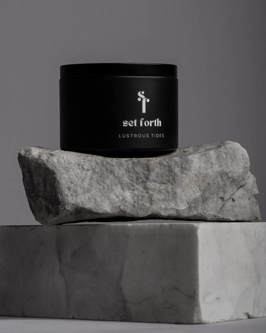 Lustrous Tides candle in matte black tin on stacked stone and marble.